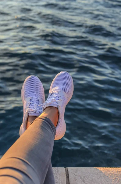 Legs in sneakers against the background of the evening sea. — Stock Photo, Image