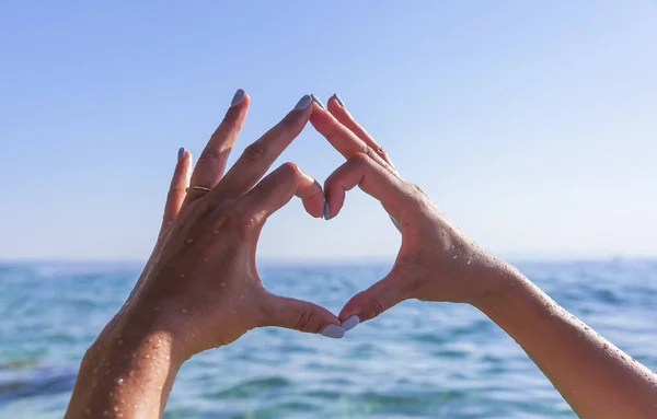 Hands in the shape of heart against the background of the sea. — Stock Photo, Image