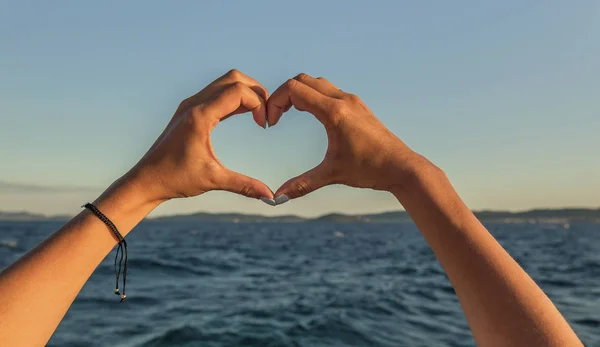 Hände in Herzform vor dem Hintergrund des Meeres. — Stockfoto