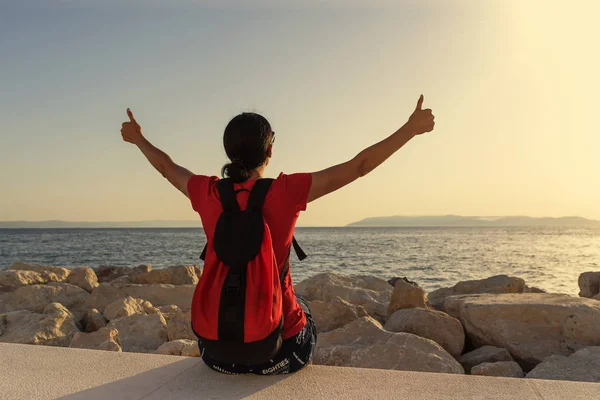 Young attractive woman showing thumbs up on hands sitting on the seashore. — Stock Photo, Image