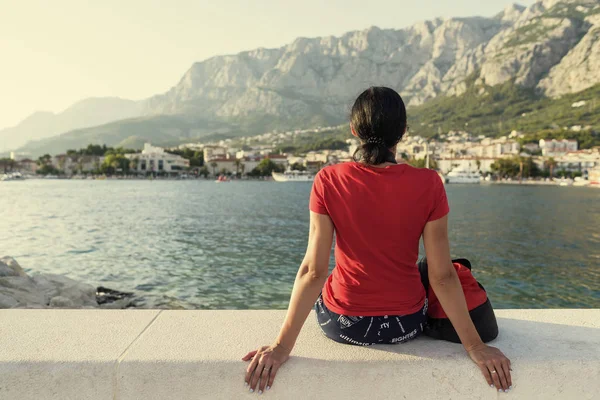 Girl sitting on a pier and watching the sunset. — Stock Photo, Image