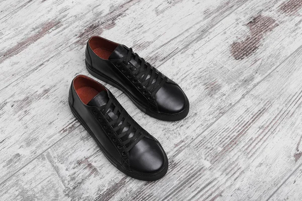 Black leather sneakers on a light laminate.