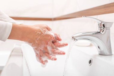 Erkek ya da kadın banyoda lavaboda dururken ellerini sabunla yıkıyor..