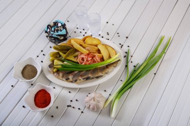 Set of fish with potato slices and onion on white plate.