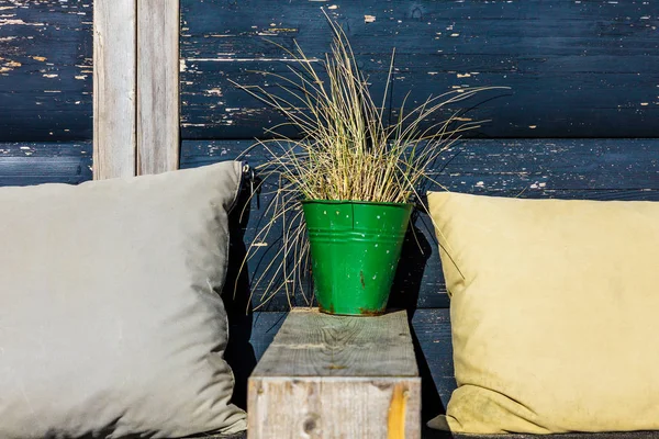 A withered yellow grass on a blue background of vintage wooden boards. Grass in a green vase with vintage pillows.