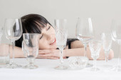Mladá žena s jinými sklenicemi na víno na stole na bílém pozadí. Spousta sklenic na pití se sluncem a stínem.