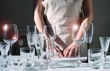 Siyah arka plandaki masada farklı şarap kadehleri olan bir kadının elleri. Güneş ışığı ve gölgesi olan içecekler için bir sürü bardak..