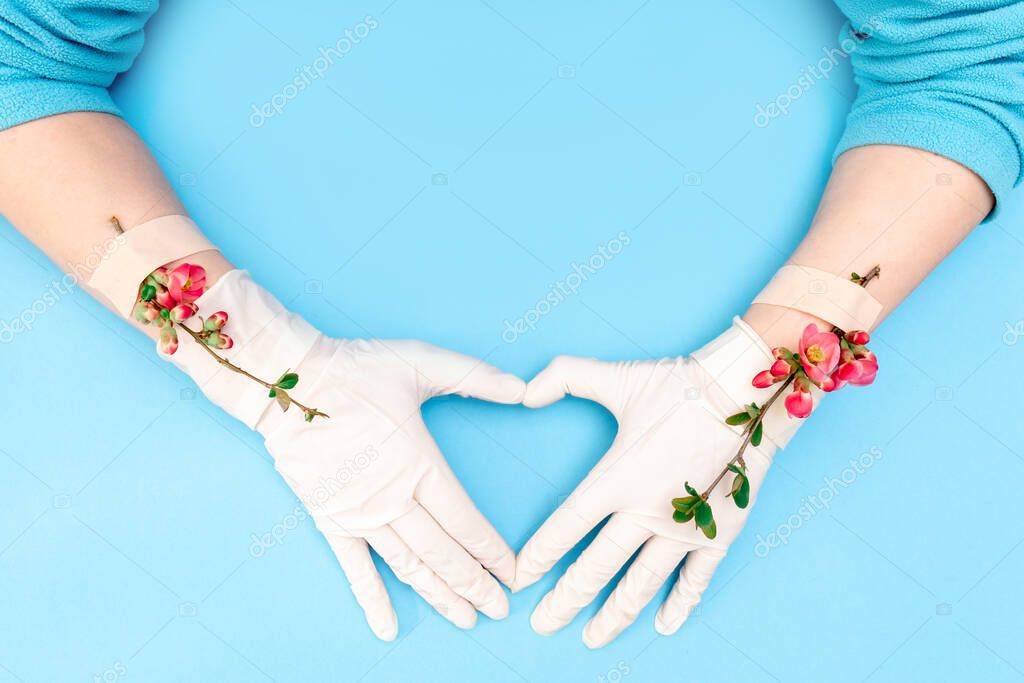 Spring pink flowers with adhesive patch on the hand with white medical glove, blue background. Concept of the end of the disease or pandemic.