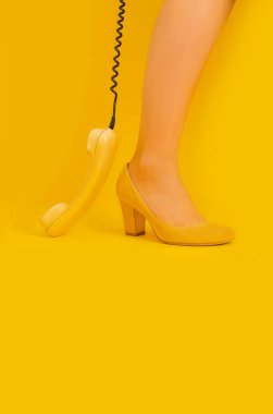 Sarı arkaplanda sarı ayakkabılı kadın bacakları ve eski sarı bir cep telefonu..