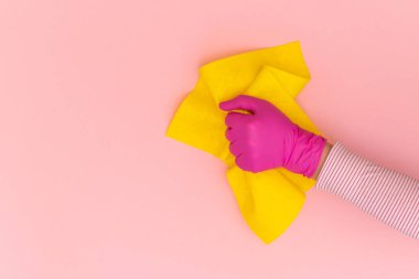 Pembe arka planda sarı silecekli pembe koruyucu eldivenli kadın eli. Üst görünüm, alanı kopyala.