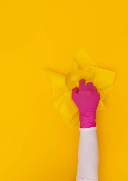Female hand in pink protective glove with yellow wiper on the yellow background. Top view, copy space.