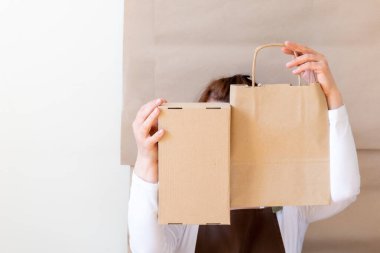 Paketçinin elleri bir Kese Kağıdı ve Kutu tutuyor. Kahverengi önlük giymiş işçiler Müşteri Paketleme Emri.