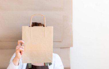Paketçinin elleri bir Kese Kağıdı ve Kutu tutuyor. Kahverengi önlük giymiş işçiler Müşteri Paketleme Emri.