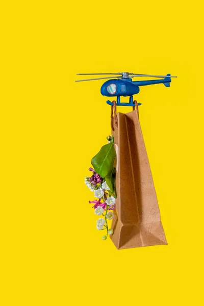 Blue Toy Helicopter Delivers Gift Paper Bag with Spring Flowers. Mother\'s day, Valentine\'s day, Birthday concept.