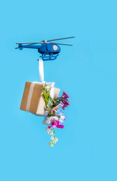 Blue Toy Helicopter Delivers Gift Paper box with flowers on the blue Background. Mother\'s day, Valentine\'s day, Father\'s day, Birthday concept.