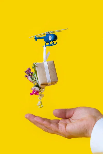 蓝色玩具直升机运送礼品盒 黄色背景上有花 母亲节 情人节 父亲节 生日的概念 — 图库照片