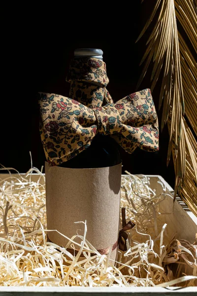 Bottle of red or white wine with Bow Tie on a black background with tropical leaves.