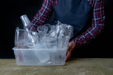 Bir sürü farklı plastik kap ve siyah arka planda ellerinde gurbage ve temizleyici olan kaplar var. Çevrenin korunması kavramı.