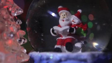 Noel Baba güzel, renkli, yeni yıl ağacının yanında, cam bir kürede oturur ve çocuklara yeni yıl için hediyeler hazırlar.