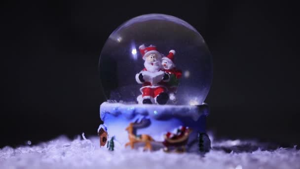 Santa y su ayudante muñeco de nieve, en una bola de cristal, lee una lista de regalos para los niños para las vacaciones de Navidad — Vídeos de Stock