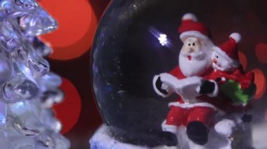 Noel Baba güzel, renkli, yeni yıl ağacının yanında, cam bir kürede oturur ve çocuklara yeni yıl için hediyeler hazırlar.