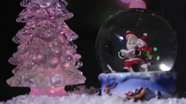 Babbo Natale vicino a un abete bello, colorato, di anno nuovo, si siede in una sfera di vetro e prepara regali per bambini durante anno nuovo — Video Stock