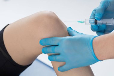 Doktor hastanın diz eklemine bir enjeksiyon yapıyor. Dize bir kurşun.