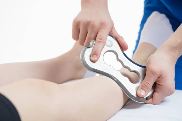 Doktor bıçak aletini kullanarak masaj yapıyor. Bacağındaki yumuşak dokuların hareket kabiliyeti artmış. Beyaz arkaplan, izole et