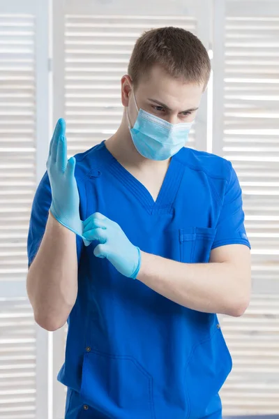 A doctor in a medical mask prepares for work and puts on medical gloves