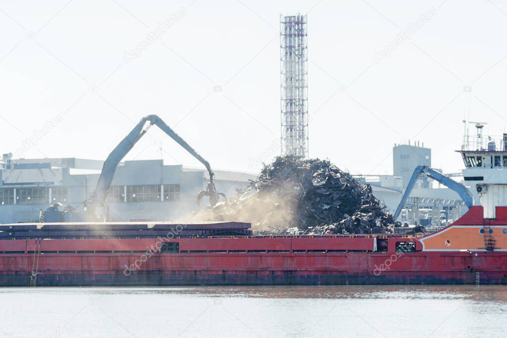 in port loading and unloading scrap metal on a barge