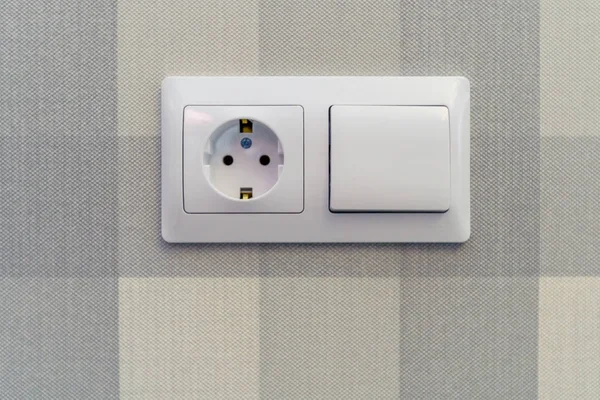 Socket and switch white on the background of paper Wallpaper on the wall. Background-vertical and horizontal blue stripes of different saturation. Texture units of flax.