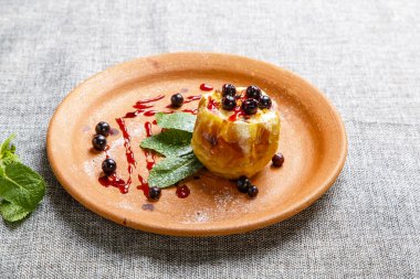 Yaban mersinli fırında elma. Bir kil tabağı. Yakında nane yaprakları var..  