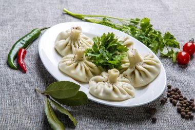 Gürcistan usulü khinkali ve bir tabak dolusu maydanoz. Tabak gri bir tuval üzerinde yatıyor.. 