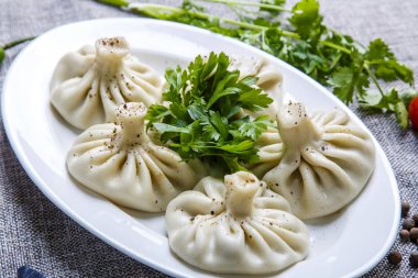 Gürcistan usulü khinkali ve bir tabak dolusu maydanoz. Tabak gri bir tuval üzerinde yatıyor.. 