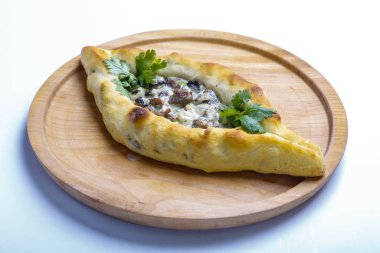 Et ve mantarlı Khachapuri teknesi. Malzemeler: sığır filetosu, mantar, krema sosu, bitkiler. Khachapuri yuvarlak ışıklı ahşap bir tahtada servis edilir.. 