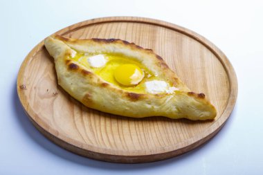 Sıcak ve lezzetli Gürcü khachapurusu. Tekne şeklinde. Yumurta ve tereyağlı peynir. Khachapuri yuvarlak ışıklı ahşap bir tahtada servis edilir. beyaz arkaplan
