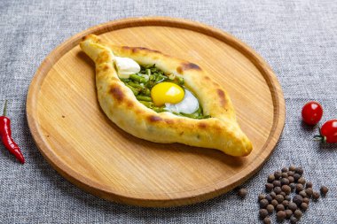 Sıcak ve lezzetli Gürcü khachapurusu. Tekne şeklinde. Yumurta ve tereyağlı peynir. Khachapuri yuvarlak ışıklı ahşap bir tahtada servis edilir. resim gri bir tuval