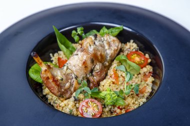 Yuvarlak siyah tabakta pirinçli kızarmış tavşan bacağı. Garnitür yeşillik ve domatesle süslenir.. 