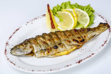 Beyaz tabakta limon ve marullu ızgara alabalık. Beyaz arkaplanda