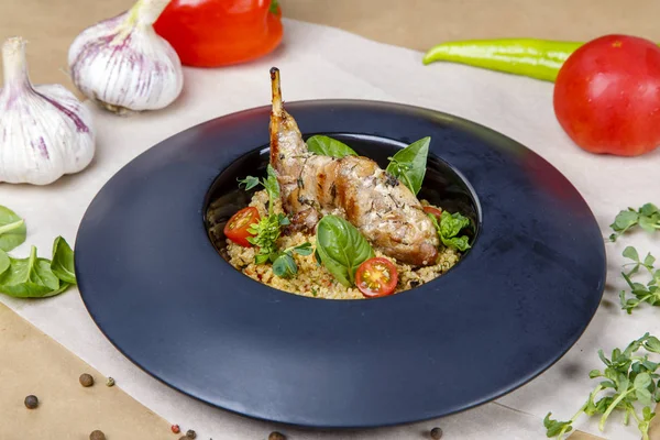 Pierna de conejo frito con arroz en un plato negro redondo. Decorar está decorado con verduras y tomates . —  Fotos de Stock