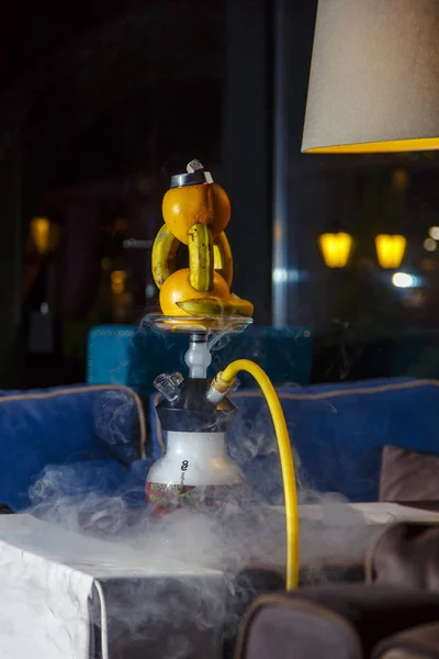 Hookah with a round transparent flask in which there is a red liquid. Hookah bowl of oranges. Lots of smoke. Black background. Yellow mouthpiece — 图库照片