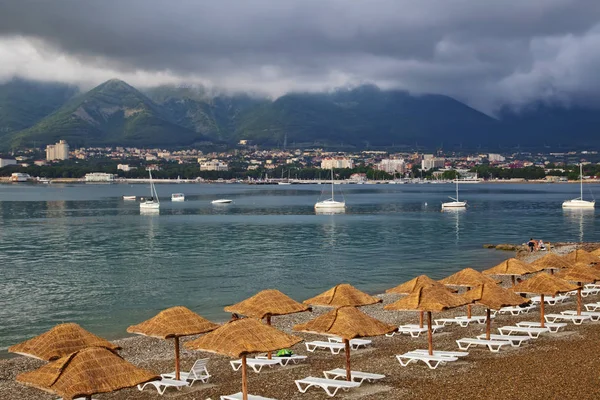 Evening in Gelendzhik Bay. In the foreground is a pebble beach, sun loungers and straw umbrellas from the sun. In the Bay in the Parking lot of the yacht. In the background mountains. — Stock Photo, Image