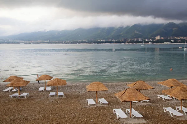 Evening in Gelendzhik Bay. In the foreground is a pebble beach, sun loungers and straw umbrellas from the sun. In the Bay in the Parking lot of the yacht. In the background mountains. — Stock Photo, Image