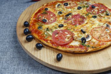 Dilimlenmiş sosisli, peynirli, zeytinli ve domatesli pizza. Hafif ahşap tabakta pizza.. 