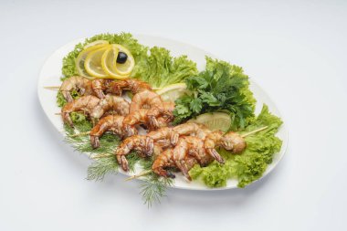 Beyaz bir tabakta marul yaprağı üzerinde Kral karidesler. Limon, zeytin ve maydanozla süslenmiş..