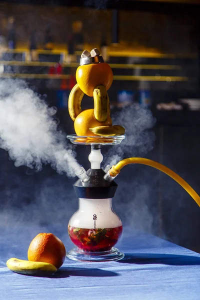 Hookah on oranges and bananas. Citrus hookah. Hookah with round clear bulb with a red liquor. A bowl of hookah made of oranges, in which bananas are inserted.