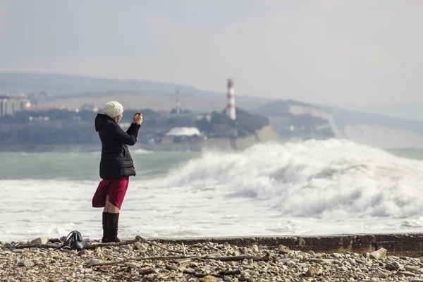 Una chica fotografía grandes olas de tormenta en el fondo de un faro y rocas . — Foto de Stock