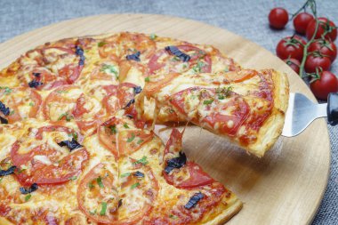 Dilimlenmiş sosisli, peynirli, zeytinli ve domatesli pizza. Hafif ahşap tabakta pizza. Pizza parçalara ayrılmış, biri diğerinden uzaklaştırılmış..