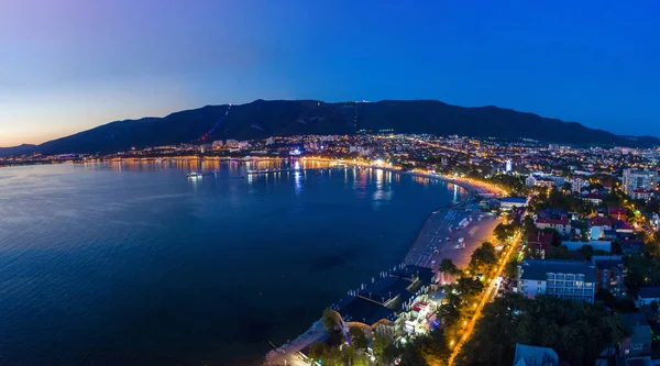 Gelendzhik sahil beldesinin akşam manzarası. Güneş battı, koyu mavi gökyüzü ve deniz. Visible Bay, plaj ve ışıklarda gezinti. Şehir çok güzel aydınlatılmış.. 