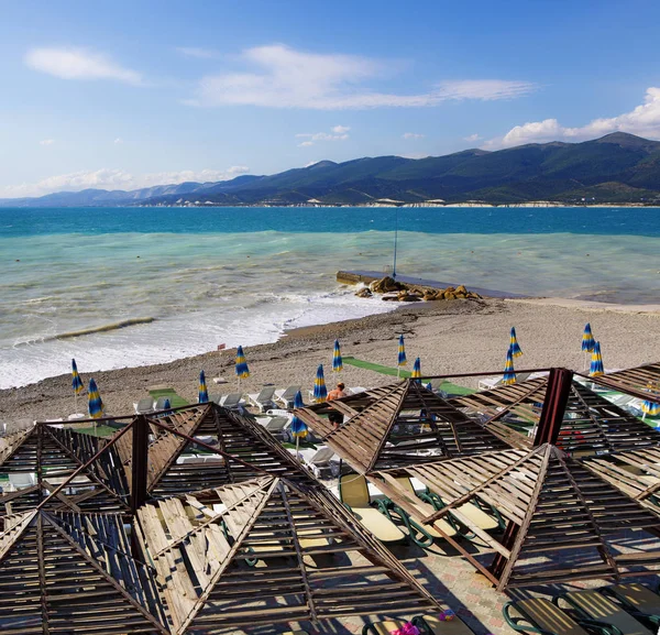 Sun loungers and umbrellas on the pebble beach in the resort of Kabardinka, Krasnodar region, Black sea. Waves and surf on the beach. — Stock Photo, Image